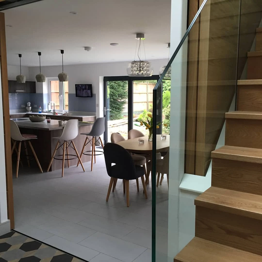 Open-plan kitchen and stairs extension with pendant lighting and a glass balustrade, finished