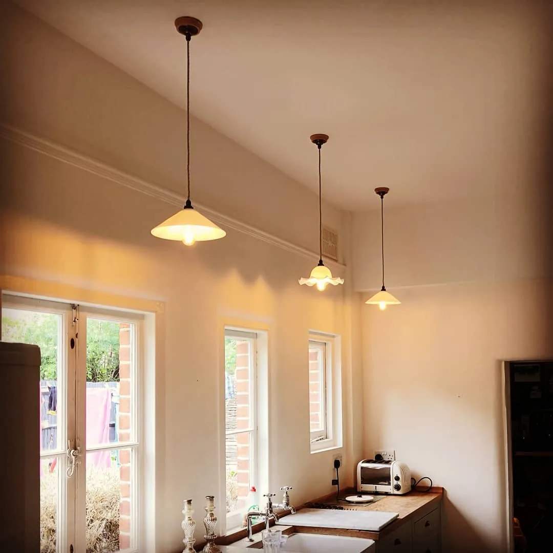 Three vintage glass pendant shades installed above a kitchen sink run